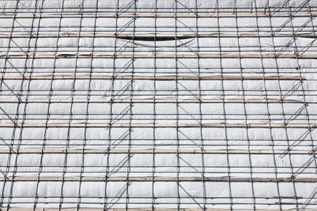 white cloth and metal poles of scaffolding against facade of high new buildingの写真素材