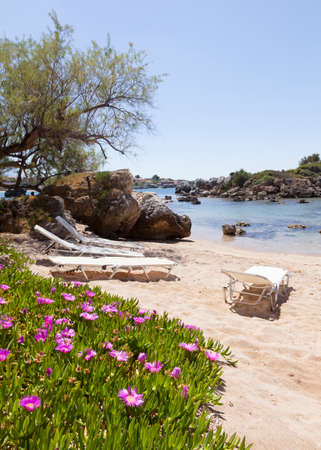 beautiful beach of Stoupa in greece on sunny day in spring on peloponnese with flowers and sunbeds and village in the backgroundの写真素材