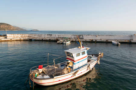 small fishing boats in harbor of agios nicolaos on greek peloponnese with sea and mountains in the background on sunny evening in aprilの写真素材