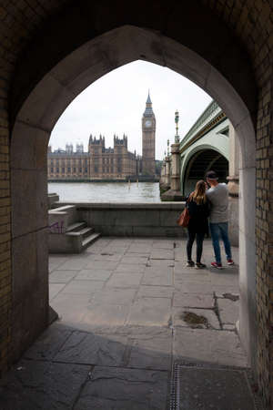 young couple on thames embankment under westminster bridge with houses of parliament and big ben in...