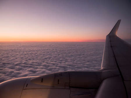 cloudscape with colorful sundown seen behind wing of airplaneの写真素材