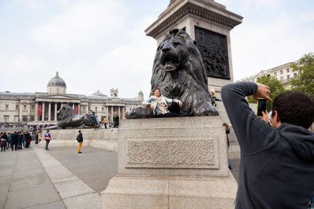 London, United Kingdom, 6 may 2017: tourist girl poses with lion statue on trafalgar square in london with national gallery in the backgroundのeditorial素材
