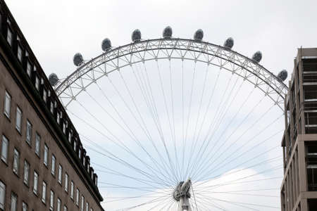 london eye between large buildings directly behind it on overcast day in springの写真素材