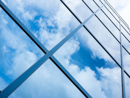 reflections of blue sky and clouds in glass facade of modern office building with diagonal linesの写真素材