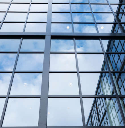 reflections of blue sky with clouds and other building in glass facade of modern office buildingの写真素材
