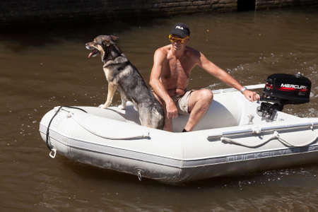 Leeuwarden, Netherlands, 11 june 2017: tanned man wearing sunglasses rides with his dog in motorized rubber boat on sunny day in summerのeditorial素材