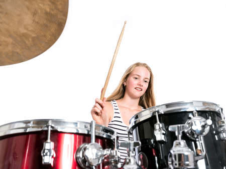 young blond caucasian teenage girl plays the drums in studio against white backgroundの写真素材
