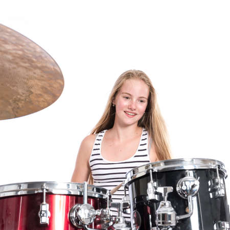 young blond caucasian teenage girl plays the drums in studio against white backgroundの写真素材