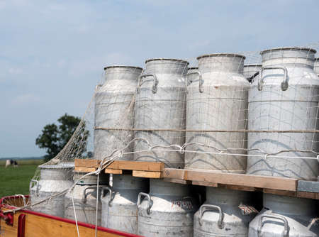 Milk churns on old vintage truck against blue sky background and meadow with cowの写真素材