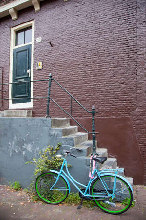 old locked blue and green bicycle in downtown amsterdam alley near stairs and brown brick wall.の写真素材