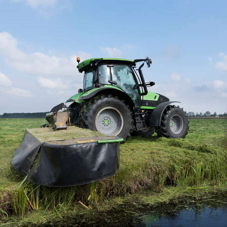 farmer mows green grassy meadow in landscape near utrecht in holland under blue skyの写真素材