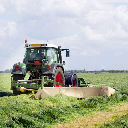 tractor and mower in green meadow in the netherlands on sunny dayの写真素材