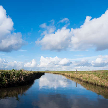 meadow landscape with canal and blue sky with clouds in the netherlands