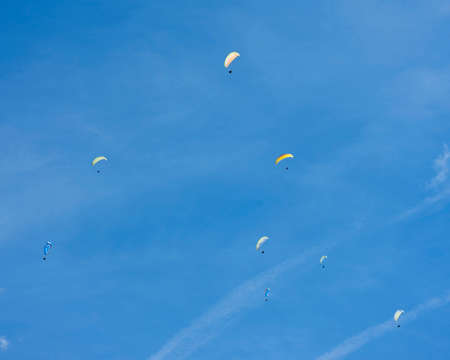 colorful paragliders in expanse of blue sky and white cloudの写真素材