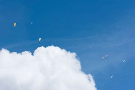 colorful paragliders in expanse of blue sky and white cloudの写真素材
