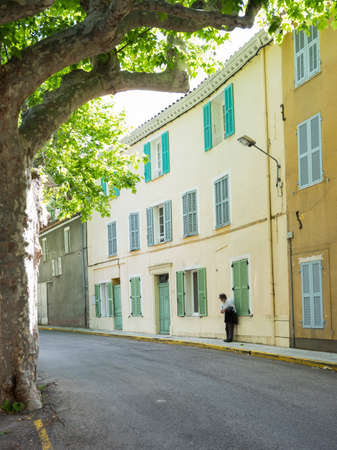 bargemon, france, 13 june 2018: man wears hat and leans against yellow wall in the old medieval french provence town of bargemonのeditorial素材