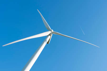 white wind turbine against blue sky and planeの写真素材