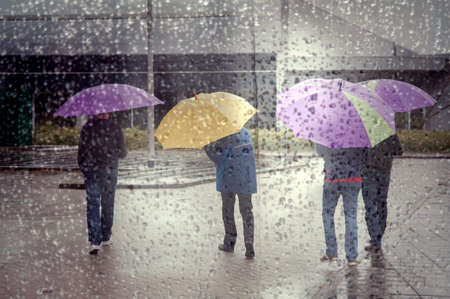 four people under colorful umbrellas seen through window full of raindropsの写真素材