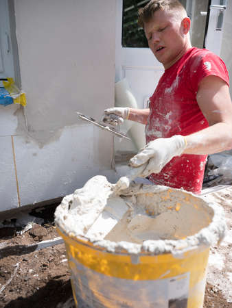 plasterer in red shirt works on white plaster of old house during insulation workの写真素材