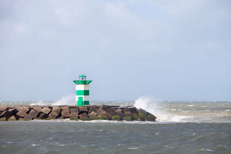 water splashes over lighthouse and pier near scheveningen harbor in the netherlands during summer stormの写真素材
