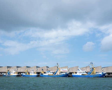 blue fishing boats lie in scheveningen harbor on stormy summer day in the netherlandsの写真素材