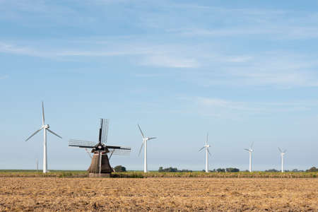 old windmill in field and modern turbines in dutch province of friesland under blue sky in summerの写真素材