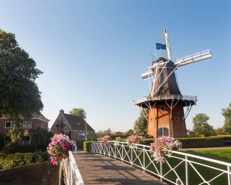 flowers on bridge and old windmill in dutch town of dokkum on sunny summer morningの写真素材