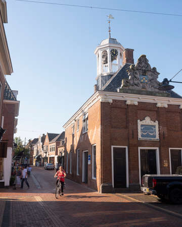 dokkum, netherlands, 24 august 2019: woman on bicycle next to waag building in old frisian town of dokkumのeditorial素材