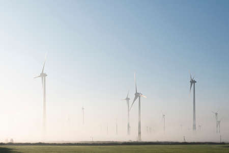 wind turbines in green meadow near aurich in german lower saxony on misty morning in augustの写真素材