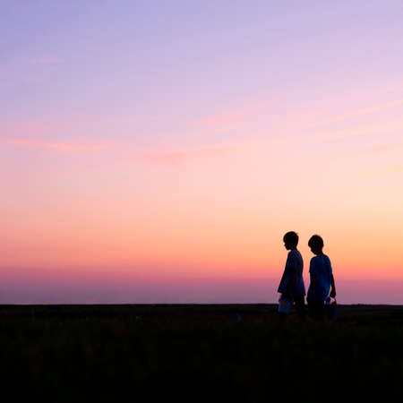 silhouette of two young boys with buckets against colorful sunsetの写真素材