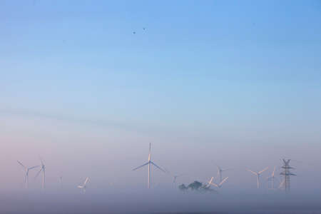 wind turbines in early morning mist on countryside of german ostfriesland in lower saxony under blue...