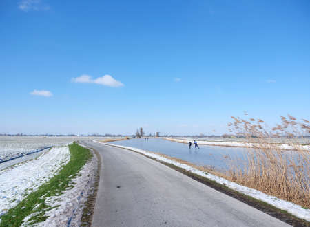 people skate on the ice on canal in alblasserwaard under blue skyの写真素材