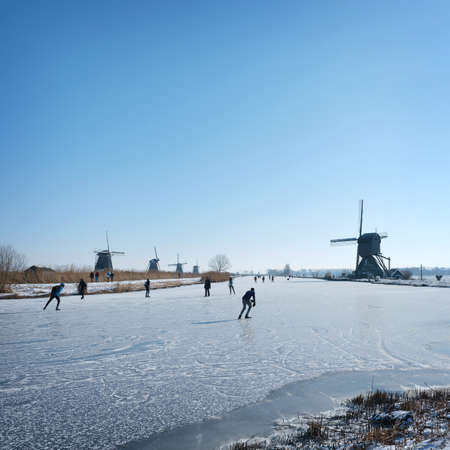 people skate on the ice near kinderdijk with al lot of windmills in holland on sunny winter dayの写真素材