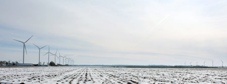 snow covered fields and farm in dutch polder of flevoland under blue sky in winter with wind turbinesの写真素材