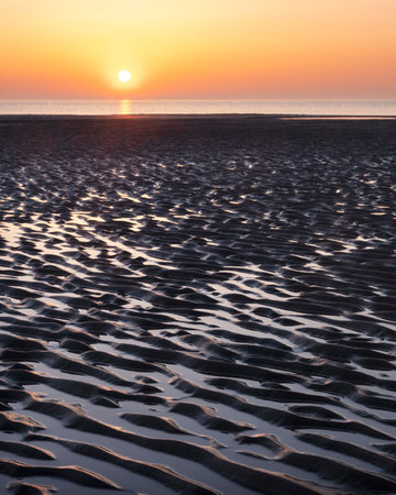 pattern in sand and colorful reflection of setting sun in water during sunset on beachの写真素材