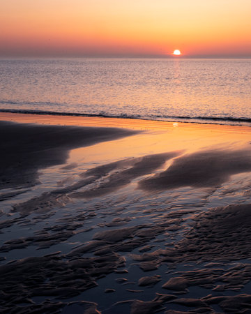 pattern in sand and colorful reflection of setting sun in water during sunset on beachの写真素材