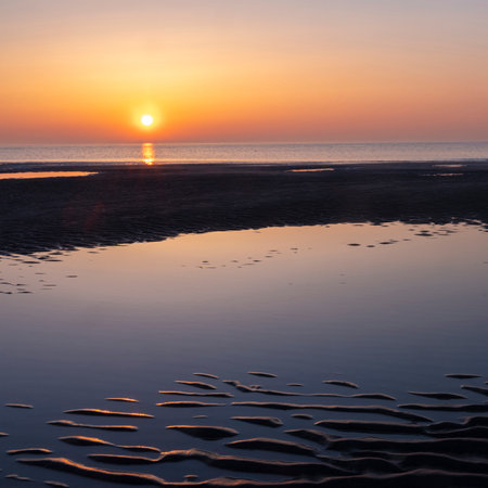 reflection of colorful sunset in water near beach on the Dutch coast in Hollandの写真素材