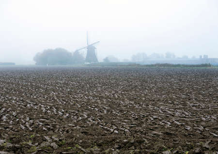 freshly plowed field and silhouette of windmill in the netherlands during fallの写真素材