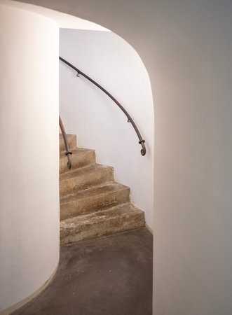bottom steps of winding concrete staircase in old building with white walls and iron railingの写真素材