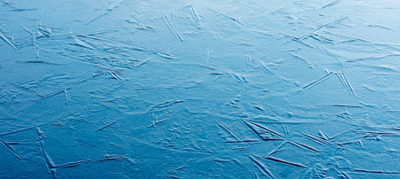 harsh graphic lines caused by grass or reed in frozen puddle reflect blue of skyの写真素材