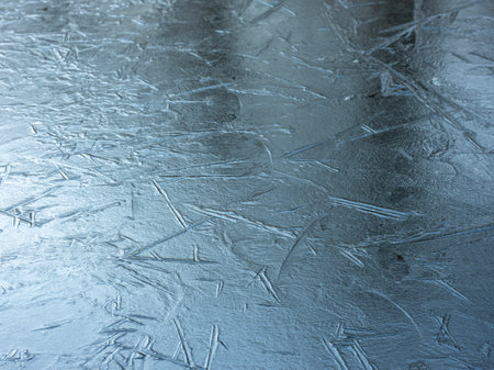 harsh graphic lines caused by grass or reed in frozen puddle reflect blue of skyの写真素材