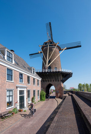 neighborhood near duurstede, netherlands, april 20, 2025: people pass windmill on sunny spring day in neighborhood near duurstede near utrecht in hollandの写真素材