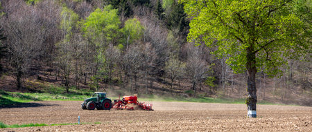farmer harrows land near clervaux in luxembourg in spring with forest in the beckgroundの写真素材