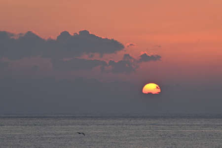 The sun rising through the clouds above the seaの写真素材
