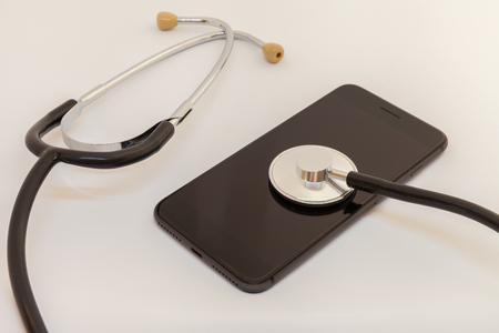 stethoscope is leaning against the screen of a black smartphoneの写真素材