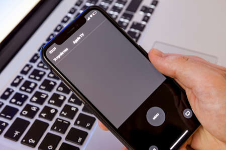 Moscow / Russia - April 4, 2020: iPhone 11 pro in hand on a macbook keyboard background. On-screen remote control application for apple tvのeditorial素材