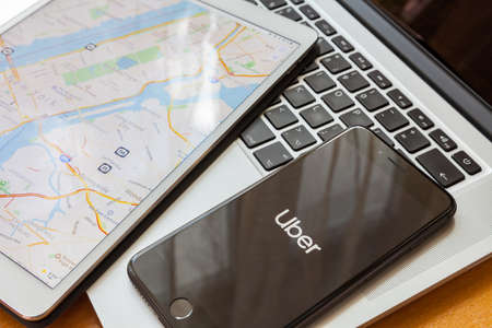 Moscow / Russia - March 13, 2019: A black iPhone lies on the MacBook. On the screen is the Uber logo. Nearby is an iPad with a map of New Yorkのeditorial素材