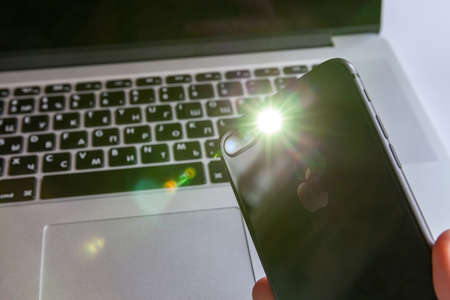 Moscow / Russia - April 5, 2019: A black iPhone holds a flashlight in its hand against the background of a MacBookのeditorial素材