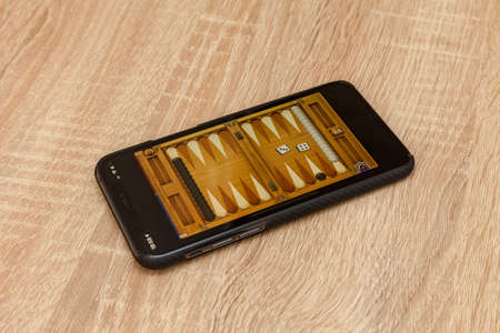 Moscow / Russia - March 26, 2020: Black iPhone 11 pro lies on the table. Backgammon game on the...