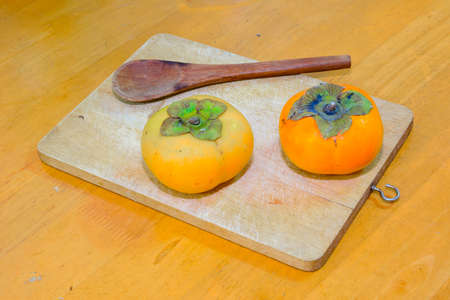 Two persimmon and Wood Spoon on the chopping blockの写真素材